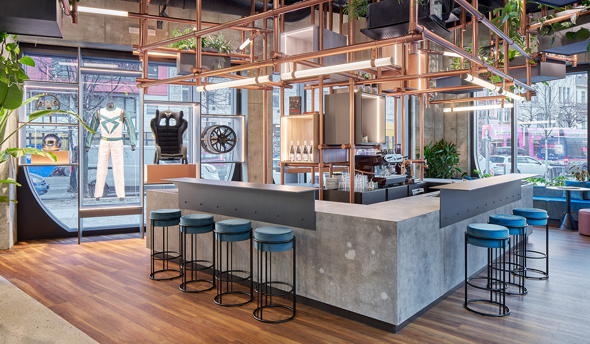 Barbereich der CUPRA City Garage mit zentralem Tresen, Hockern und bodentiefen Fenstern in seitlicher Perspektive